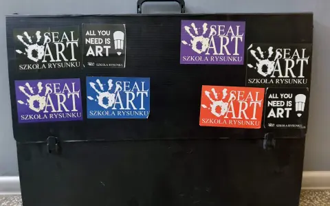 Czarna walizka na prace plastyczne ozdobiona naklejkami "SEAL ART SZKOŁA RYSUNKU" i "ALL YOU NEED IS ART".