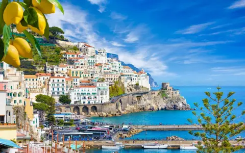 Costiera Amalfitana, un sogno di **Italia in moto** tra limoni e mare blu. Case bianche aggrappate alla roccia, un borgo pittoresco.
