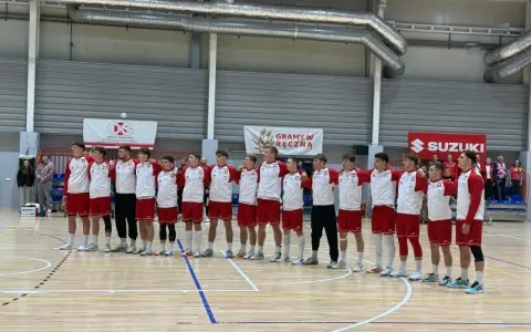 Drużyna w strojach biało-czerwonych, w tym Filip Jankowski, stoi na parkiecie hali sportowej.