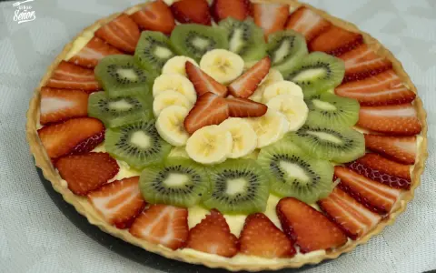 Deliciosa tarta con decoración de tartas con frutas: fresas, kiwi y plátano, dispuestas en círculos concéntricos sobre una base cremosa.