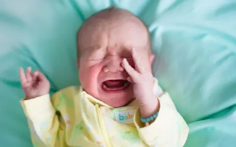 Ein **baby weinen** auf einem türkisfarbenen Tuch, mit geschlossenen Augen und einer Hand vor dem Gesicht.