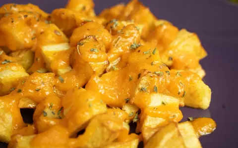 Patatas bravas crujientes cubiertas con una salsa naranja cremosa y hierbas picadas.