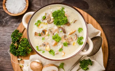 Kremowa zupa pieczarkowa, przepis babci, z kawałkami pieczarek i natką pietruszki. Obok miseczka z solą i świeże pieczarki.