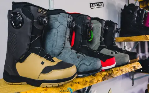 Rząd butów snowboardowych w różnych kolorach i stylach, ustawionych na drewnianej półce.