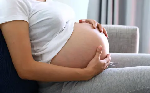 Kobieta w ciąży trzyma dłonie na brzuchu, zastanawiając się, jak przyspieszyć poród.