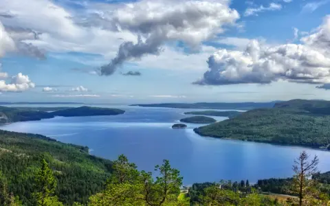 Vacker utsikt över en sjö med öar, omgiven av skogklädda berg. Ett perfekt ställe att uppleva Stockholms naturreservat.