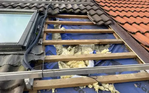 Uszkodzony dach z widoczną izolacją, jakby kuna zrobiła sobie tam gniazdo.