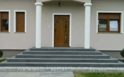 Elegancka, zewnętrzna klatka schodowa w domu jednorodzinnym prowadzi do brązowych drzwi z witrażem.