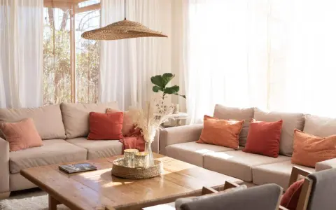 Salones pequeños con encanto: sofás beige, cojines terracota y naranja, mesa de madera, plantas y luz natural.