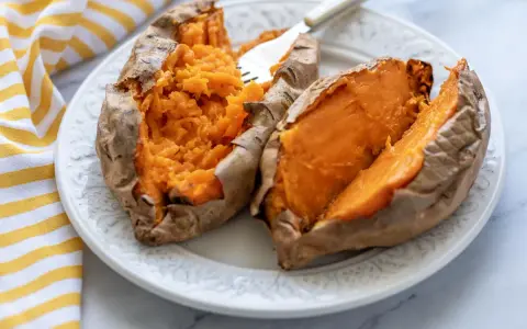 Boniato tierno y esponjoso hecho en air fryer, servido en plato blanco con un tenedor.