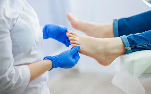 Podolog w niebieskich rękawiczkach bada stopę, która cierpi na ból palców u nóg.