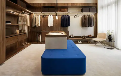 En lyxig walk-in-closet med mörka trädetaljer och en blå sittbänk, allt i en elegant italiensk stil.