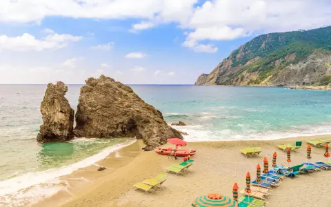 Spiagge sabbia Liguria: scogli imponenti, mare turchese e lettini pronti per il relax.