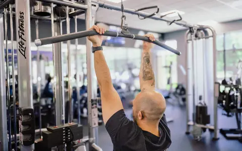 Man med tatueringar utför enarms latsdrag på ett gym.