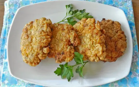 Cuatro filetes rusos dorados y crujientes servidos en un plato blanco con perejil.