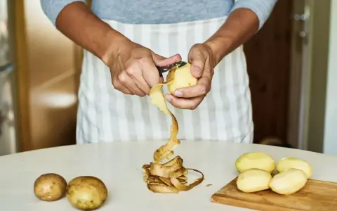 Mani che sbucciano patate per la cottura. Il tempo di cottura patate lesse senza buccia è breve.