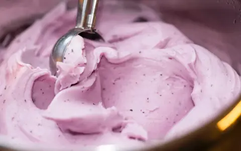 Ein Löffel nimmt eine Portion cremiges, kalorienarmes Eis mit Beerenstücken auf.