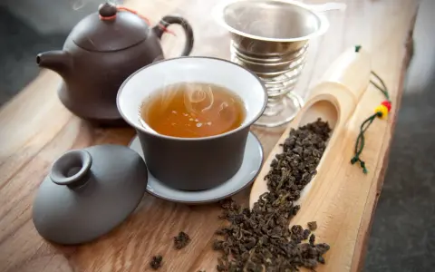 Dampfender Oolong Tee in einer Tasse, daneben Teekanne, Sieb und lose Teeblätter. Die Oolong Tee Wirkung kann belebend sein.