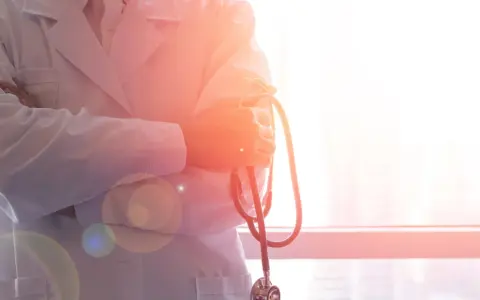 Lekarz w białym kitlu trzyma stetoskop. W tle okno z widokiem na miasto. To symbol najlepszych hematologów w Polsce.