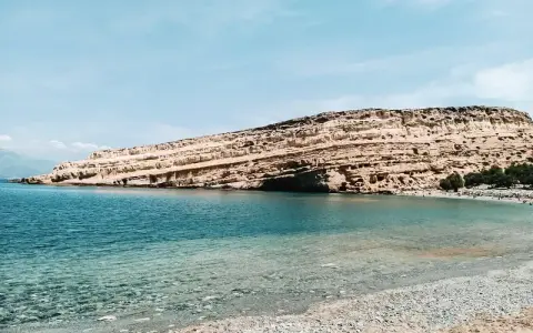 Plaża z kamienistym brzegiem i skalistym klifem w tle, nad turkusowym morzem.