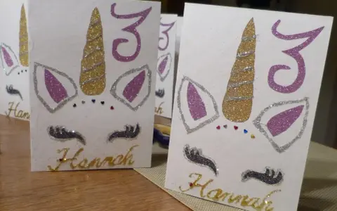 Glitzernde Einhorn-Einladungen zum 3. Geburtstag basteln. Hannahs Name ist in Goldbuchstaben geschrieben.