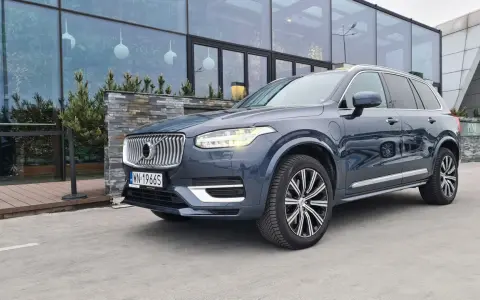 Elegancki, ciemnoszary Volvo XC90 T8 z nowoczesnymi światłami LED stoi przed budynkiem z dużymi, przeszklonymi oknami.