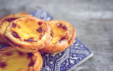 Ein Stapel goldbrauner, karamellisierter Pastel de Nata auf einer blauen Kachel.