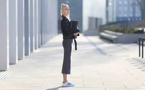 Kobieta w czarnej ramonesce i szarej spódnicy prezentuje stylowe adidas superstar stylizacje na tle nowoczesnej architektury.