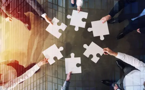 Manos unidas colocando piezas de rompecabezas, un símbolo de inteligencia colaborativa y trabajo en equipo para lograr un objetivo común.