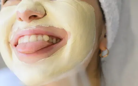 Una mujer se divierte con una mascarilla facial amarilla, sacando la lengua.