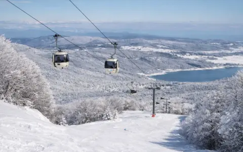 Funivia su montagne innevate, un lago azzurro sullo sfondo. Scopri dove sciare in Calabria per un'esperienza indimenticabile.