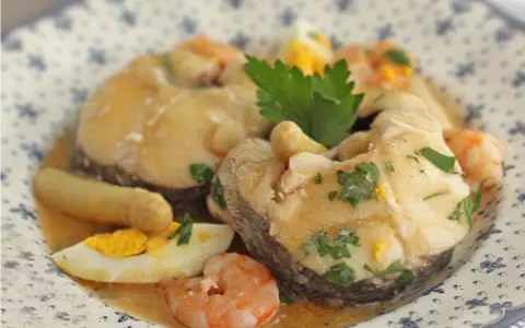 Merluza a la vasca con gambas, huevo duro y perejil, servida en un plato con diseño floral.