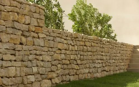 Un muret en pierre sèche, bordé d'herbe verte et de verdure luxuriante, s'étend sur la droite, menant à des marches en pierre.