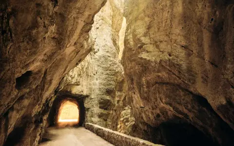 La strada della forra si snoda tra imponenti pareti rocciose, con un tunnel che si apre verso una luce accecante.