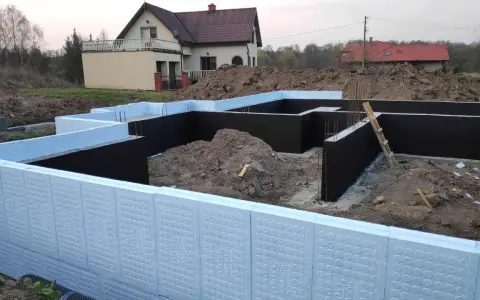Budowa domu: jak ocieplić fundament styropianem. Widoczne elementy izolacji fundamentów, zbrojenia i ziemia.