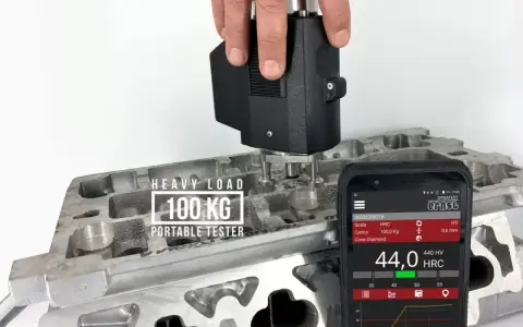 Przenośny tester z obciążeniem 100 kg mierzy twardość materiału, pokazując wyniki na skali twardości na ekranie smartfona.