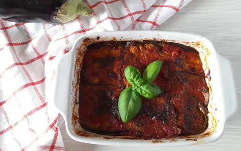 Parmigiana di melanzane non fritte, appena sfornata, guarnita con basilico fresco. La ricetta perfetta per un piatto leggero e gustoso.