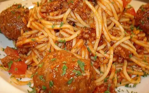 Pyszne spaghetti z pulpetami w sosie pomidorowym, posypane natką pietruszki. Klasyczne danie, które zawsze smakuje wyśmienicie.