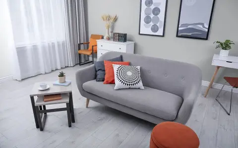 Nowoczesny salon z szarym kolorem ścian, wygodną kanapą, stolikiem kawowym i pomarańczowymi akcentami.