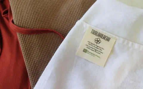 Etiqueta de **algodón orgánico que es** suave y transpirable, junto a tejidos de lino y algodón en tonos tierra.