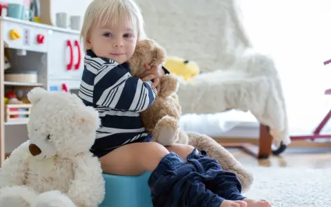 Chłopiec na nocniku, przytulający misia. To jego skok rozwojowy 18 miesiąc. Obok siedzi drugi miś.