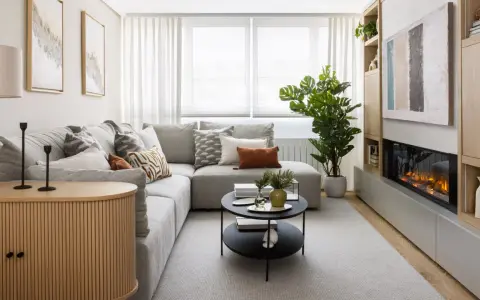 Sofá gris, mesa de centro negra, chimenea moderna y mueble de madera. Una sala acogedora, perfecta para una reforma sin obras.