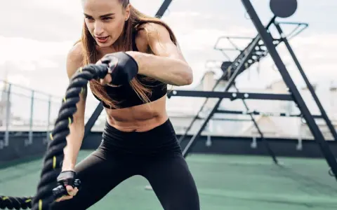 Kobieta wykonuje trening obwodowy z linami battle rope. Intensywny wysiłek buduje siłę i wytrzymałość.