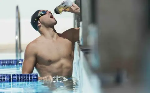 Un nageur en bonnet et lunettes boit dans une bouteille, prêt à apprendre comment nager.