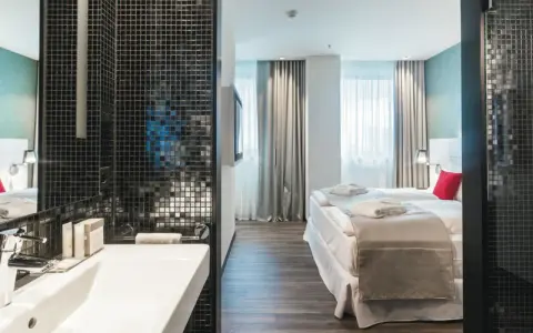 Badezimmer mit Waschbecken und Blick auf ein Hotelzimmer mit Bett und Fenstern.