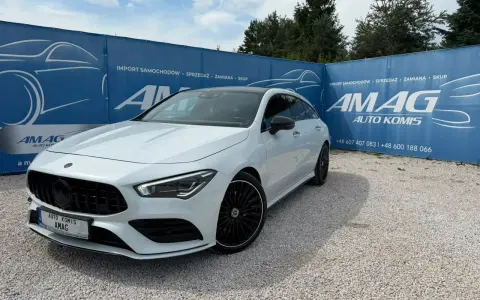 Biały Mercedes na tle niebieskiego banera AMAG Auto Komis. Idealny do akcje serwisowe Mercedes.