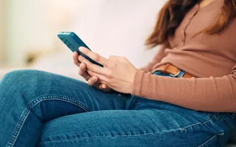 Kobieta w dżinsach i bluzce z długim rękawem trzyma telefon. To może być obraz skutków zbyt długiego korzystania z telefonu.