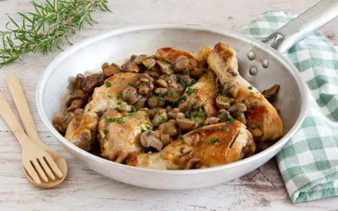 Delizioso pollo con funghi in padella, guarnito con prezzemolo fresco e accompagnato da rosmarino.