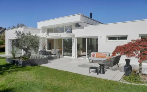 Une maison moderne avec une terrasse aménagée, un salon extérieur et un jardin. Ce projet d'extension de maison offre un espace de vie lumineux et agréable.