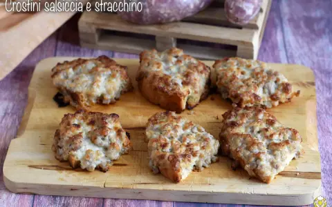 Sei crostini salsiccia e stracchino dorati e filanti, pronti per essere gustati su un tagliere di legno.